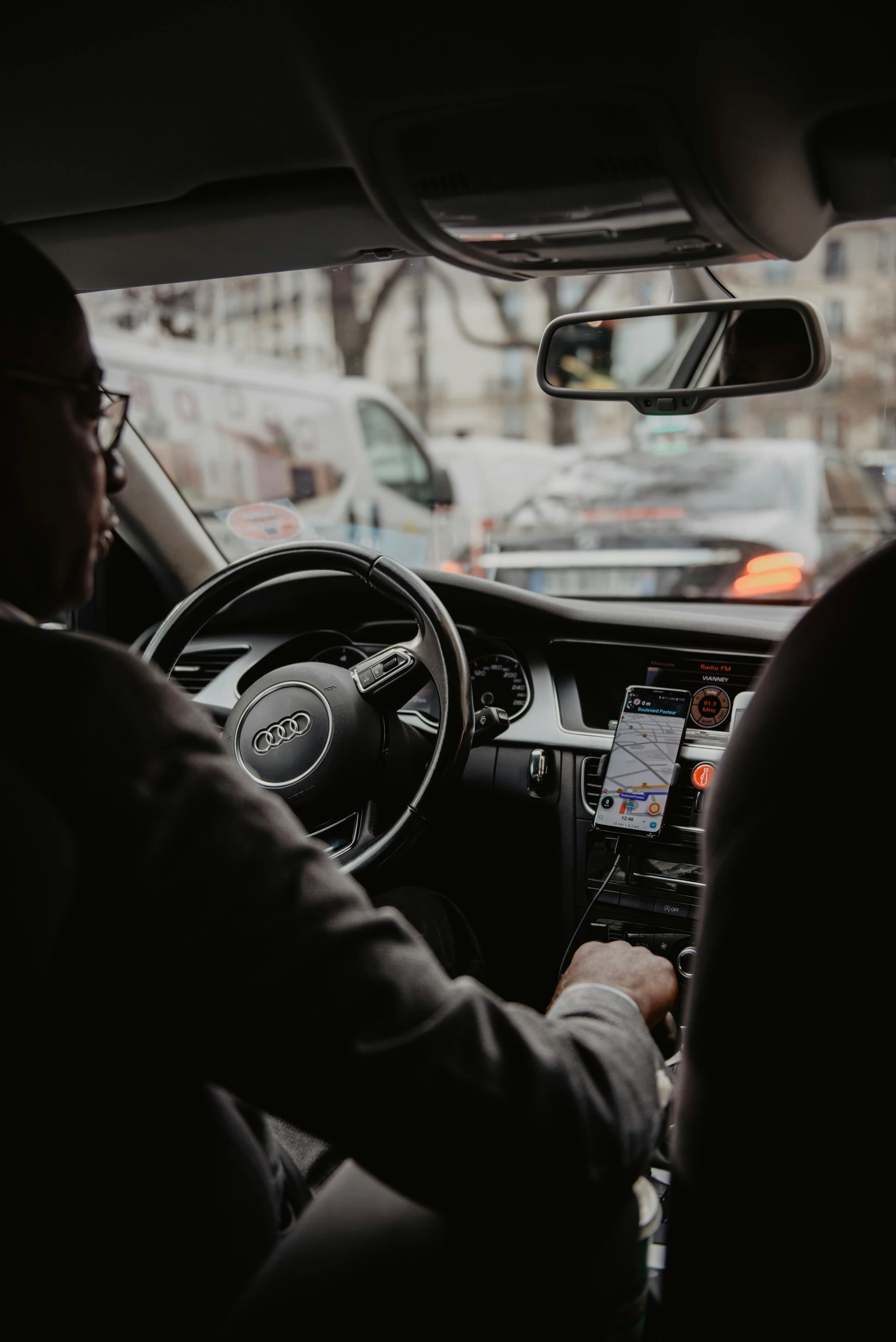 A well dressed man driving an audi in traffic, photo taken from the backseat.